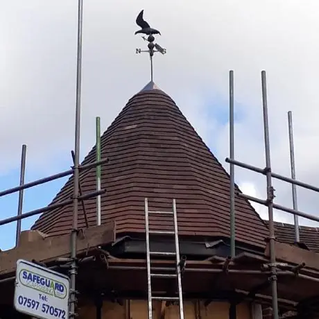 Roofing in Hindley: conical turret roof being re-tiled behind scaffolding
