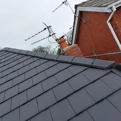 Roofing near Ashton-in-Makerfield: new grey roof tiles with dry-fit ridge beside a brick gable
